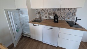 Eine kompakte Küche mit weißen Schränken, einer Kaffeemaschine und einem Geschirrspüler.