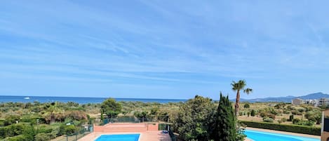 A pool area with two pools, surrounded by greenery and a view of the sea.