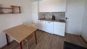 Eine kleine Küche mit Holztisch, zwei Stühlen, einem Geschirrspüler und einer Kaffeemaschine.