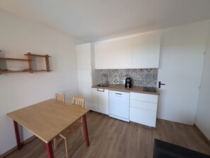 A compact kitchen with a wooden table, two chairs, a dishwasher, and a coffee maker. - Apartment with sea-facing terrace and swimming pool (Saint-Cyprien)