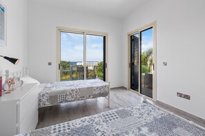 Ein Schlafzimmer mit zwei Betten, einer weißen Kommode und Meerblick durch große Fenster.