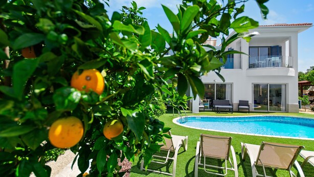 Una casa moderna con piscina, rodeada de vegetación y mobiliario de exterior.