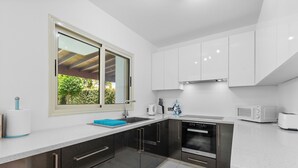 Una cocina moderna con armarios blancos, electrodomésticos de acero inoxidable y una ventana con vista a zonas verdes.