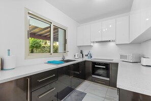 Eine moderne Küche mit weißen Schränken, Edelstahlgeräten und einem Fenster mit Blick auf Grünflächen.
