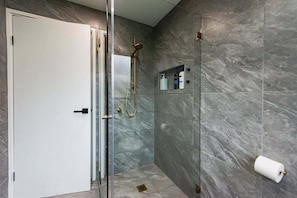 Un baño moderno con cabina de ducha de vidrio, paredes de mármol y una puerta blanca.