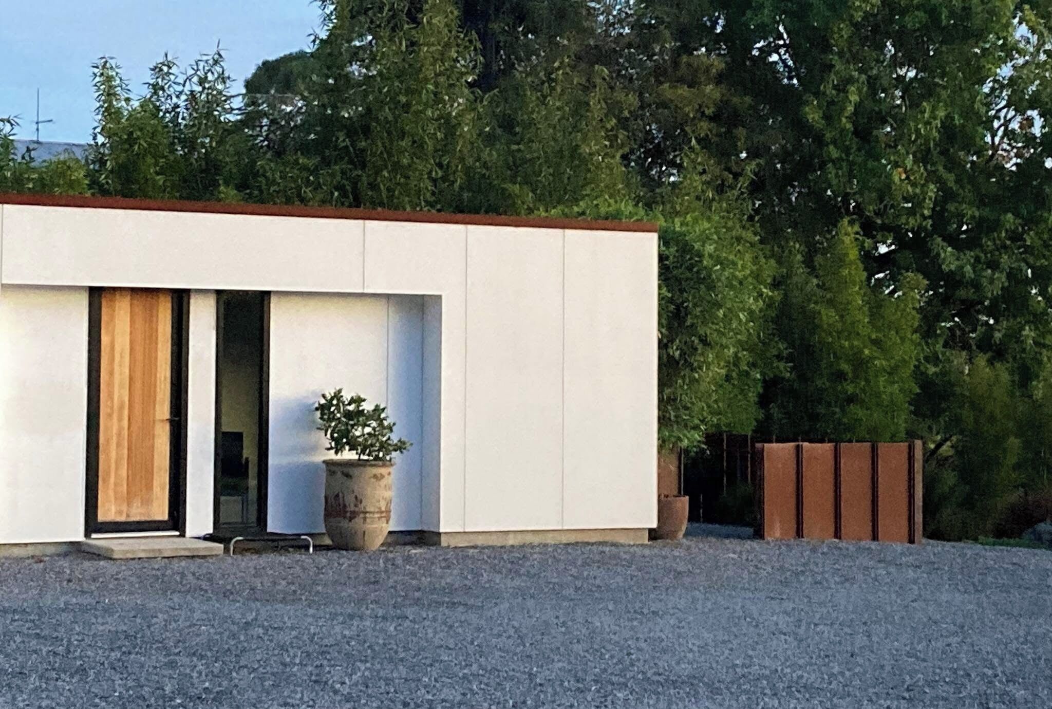 A modern building with a flat roof, large windows, and a gravel driveway.