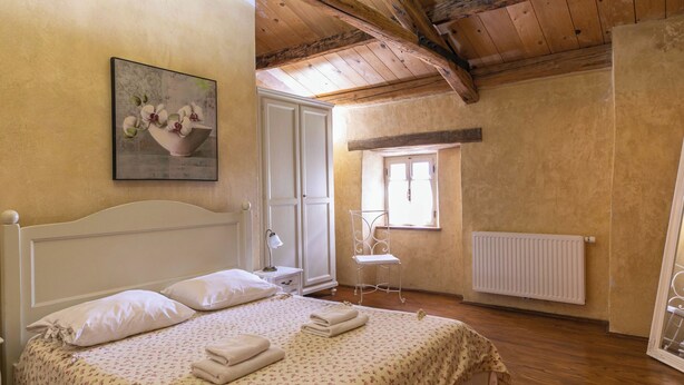 Ein Schlafzimmer mit Holzbalkendecke, einem Bett mit floralem Bettzeug, einem weißen Heizkörper und einem Fenster mit Blick.