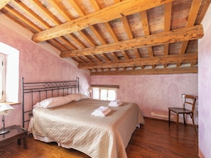 A bedroom with a wooden ceiling, a bed with a headboard, a chair, and a nightstand with a lamp. - Vacation home Altona by Interhome (Barbariga)