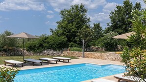 Ein rechteckiger Pool mit Steinrand, umgeben von Liegestühlen und Sonnenschirmen.