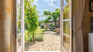 Eine geöffnete Tür, die zu einer mit Steinplatten belegten Terrasse mit Pergola, Grünpflanzen und Gartenmöbeln führt.