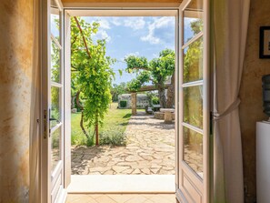 Eine geöffnete Tür, die zu einer mit Steinplatten belegten Terrasse mit Pergola, Grünpflanzen und Gartenmöbeln führt.