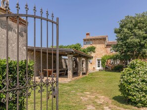 Ein Steinhaus mit überdachter Terrasse, einem Metallgitter und blauem Himmel.