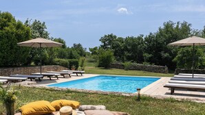 Una piscina con sillones de descanso y sombrillas, rodeada de follaje.