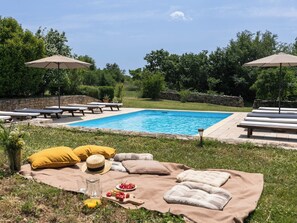 Ein Swimmingpool mit Liegestühlen und Sonnenschirmen, umgeben von viel Grün.