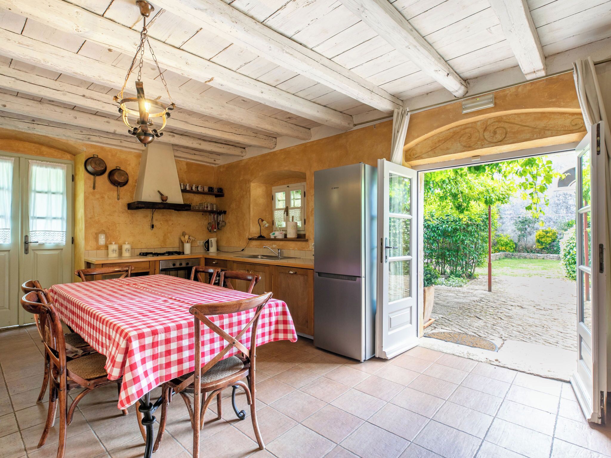 A kitchen with a dining table, chairs, a refrigerator, and a view of the garden.