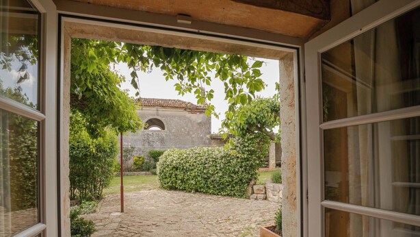 Un umbral abierto que da a un patio con un sendero adoquinado, follaje y un edificio de piedra con una entrada arqueada al fondo.