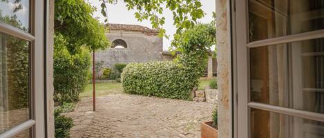 Un umbral abierto que da a un patio con un sendero adoquinado, follaje y un edificio de piedra con una entrada arqueada al fondo.