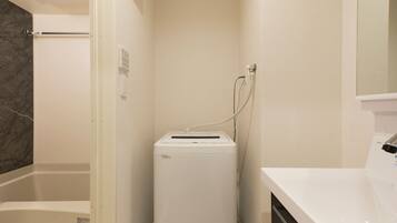 A compact bathroom with a white sink, a towel rack, a shower area, and a built-in dryer.