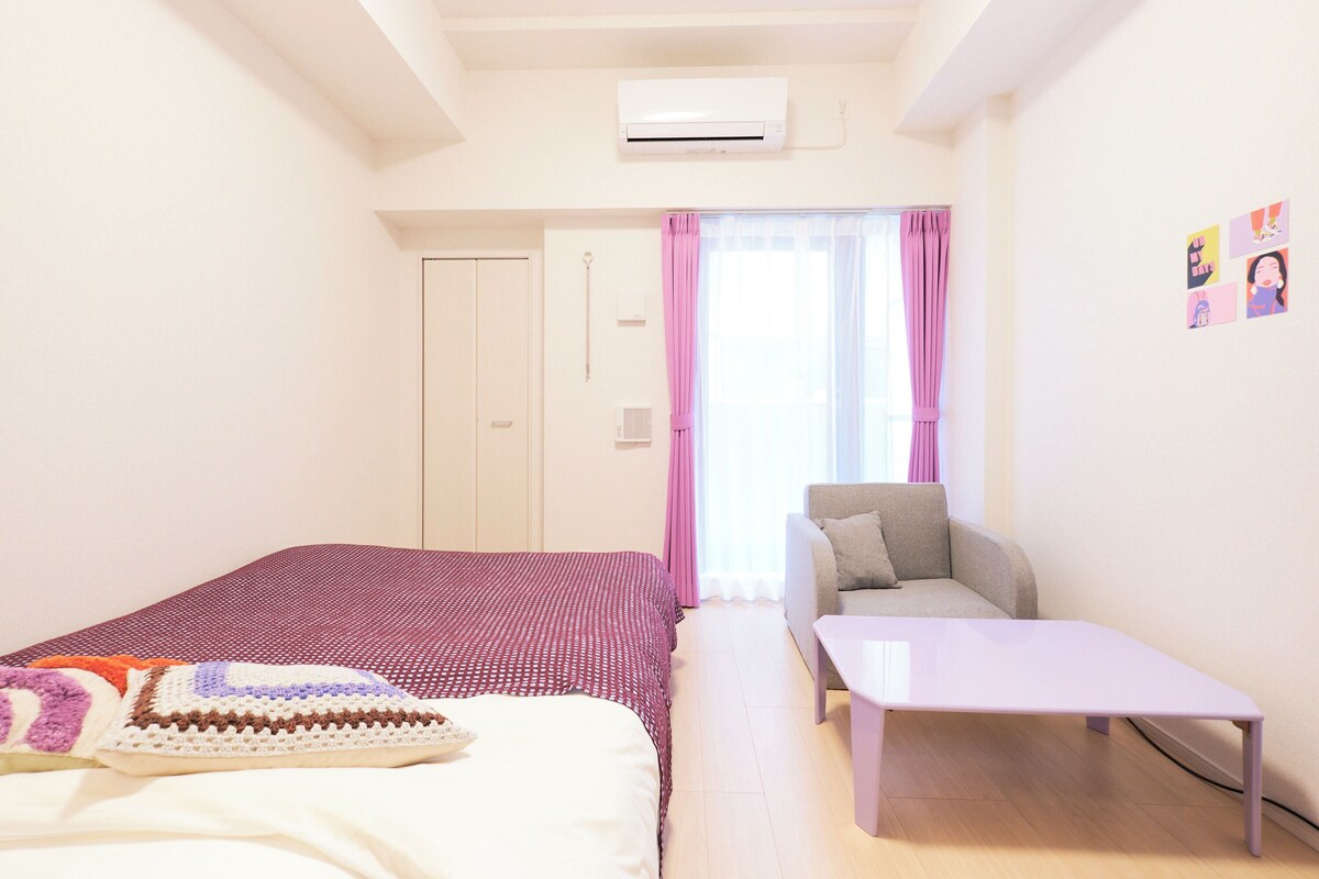 Ein Schlafzimmer mit einem Bett, einem Sessel, einem kleinen Tisch, einer Klimaanlage, einer Tür und einem Fenster mit Vorhängen.