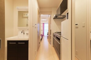 Un pasillo estrecho con una zona de cocina a la derecha, que incluye un lavamanos, estufa y armarios.