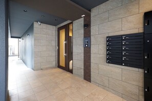 Un pasillo moderno con una zona de recepción, una puerta que da a una habitación y un buzón empotrado en la pared con compartimentos numerados.