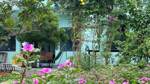 Un jardin avec des fleurs roses, un hamac et un mur de briques.