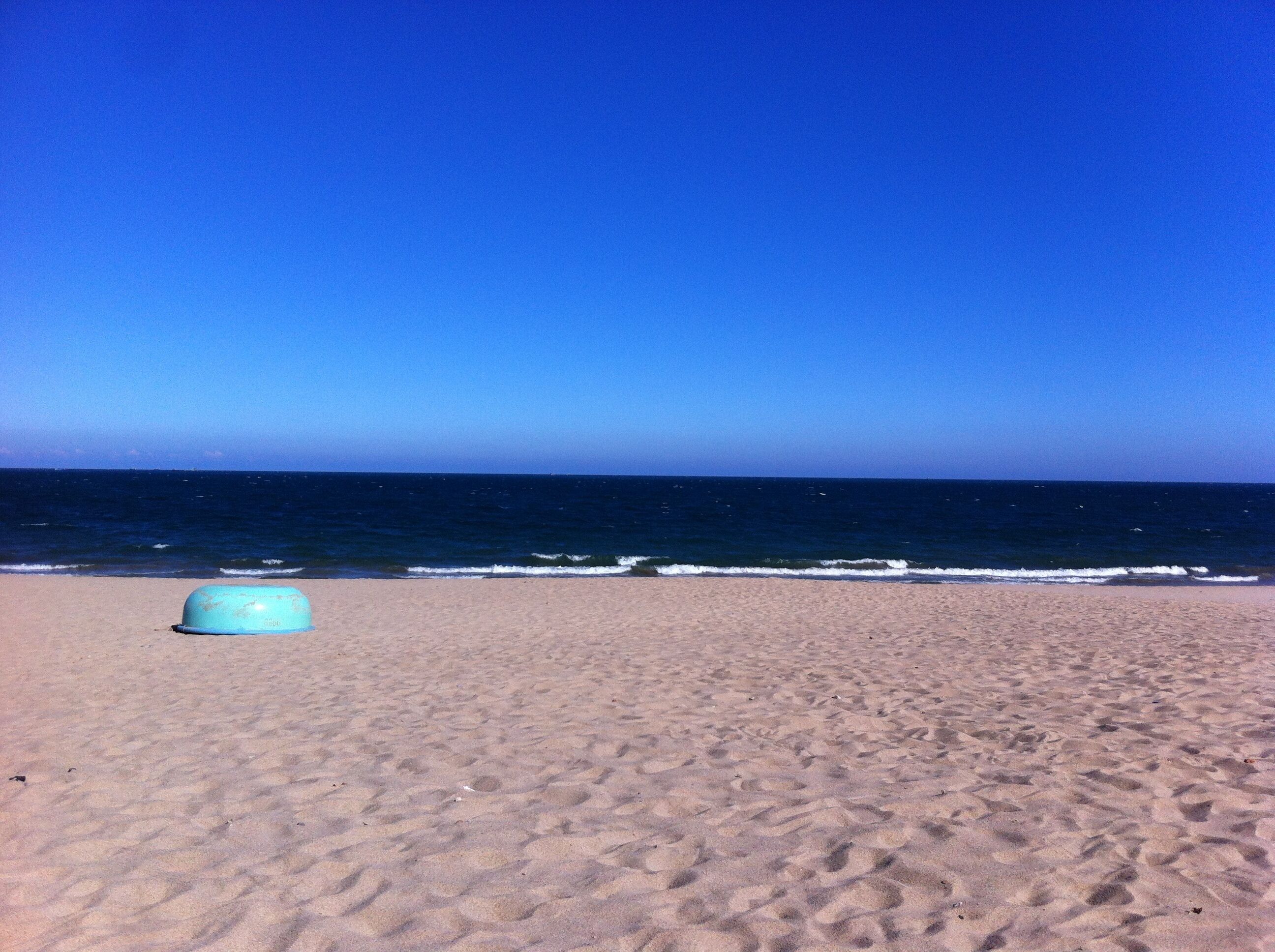 Een strand met een groot, leeg zandgebied en een helderblauwe lucht.