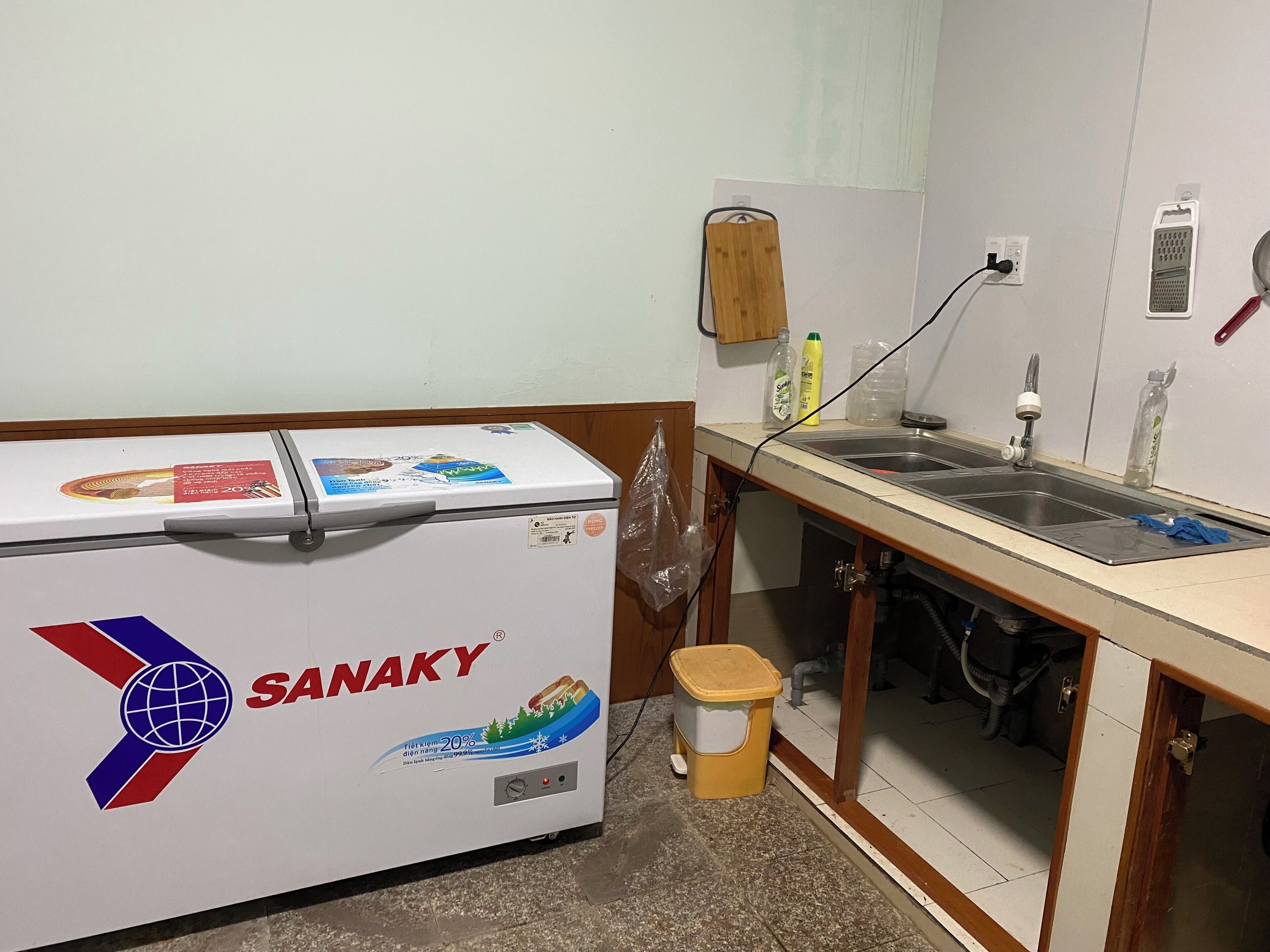 A kitchen with a refrigerator, sink, and a small trash bin.