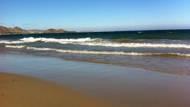 Une plage avec des vagues, du sable et des montagnes qui se dessinent à l’horizon.