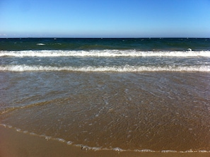 A beach with waves, clear sky, and calm sea.