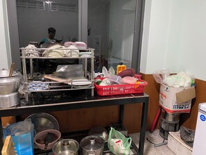 Una cocina con un estante metálico lleno de platos, una cesta roja con utensilios de cocina y un microondas.
