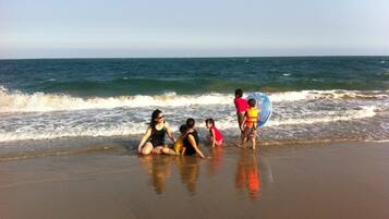 A beach scene with people sitting and standing near the water.