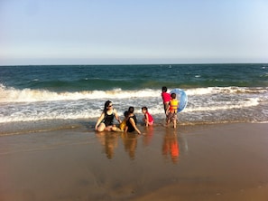 A beach scene with people sitting and standing near the water.