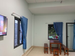 Una habitación con televisor, ventana con cortinas, mesa de madera con bancos y vistas al exterior.