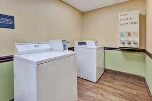 A laundry area with two front-loading washers and dryers, a soap and bleach softener dispenser, and a Hampton Inn sign. - Airport CVG 2 Queen Room Breakfast, Pool & Gym (Hebron)