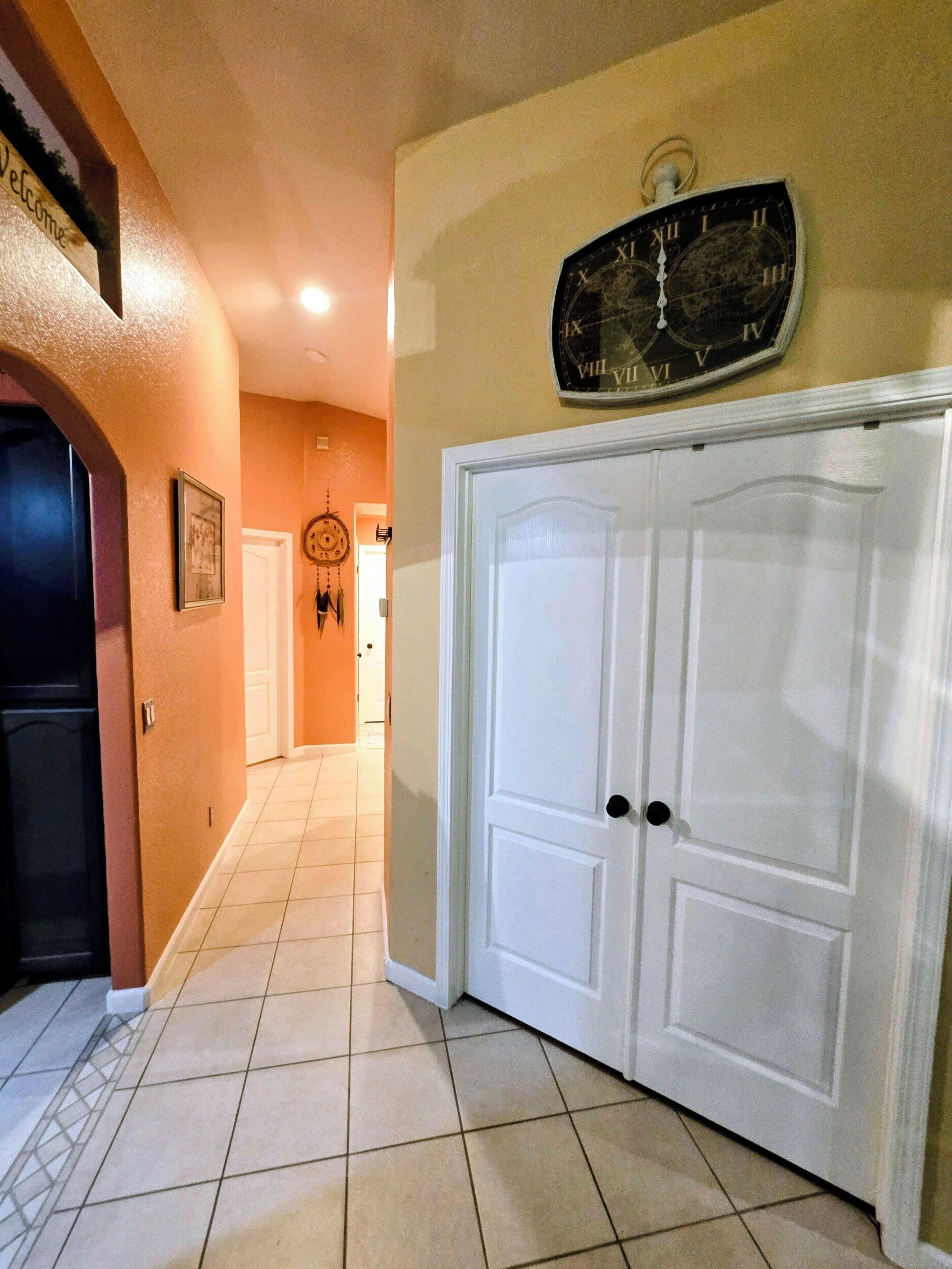 A hallway with a white door, a wall clock, and a welcome sign.
