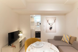 A modern living room with a flat-screen TV, a dining table set with white plates and cutlery, a sofa with patterned cushions, and a deer antler wall art. - Hotel Dieu Nakanobu by Tranova 2 (Shinagawa)