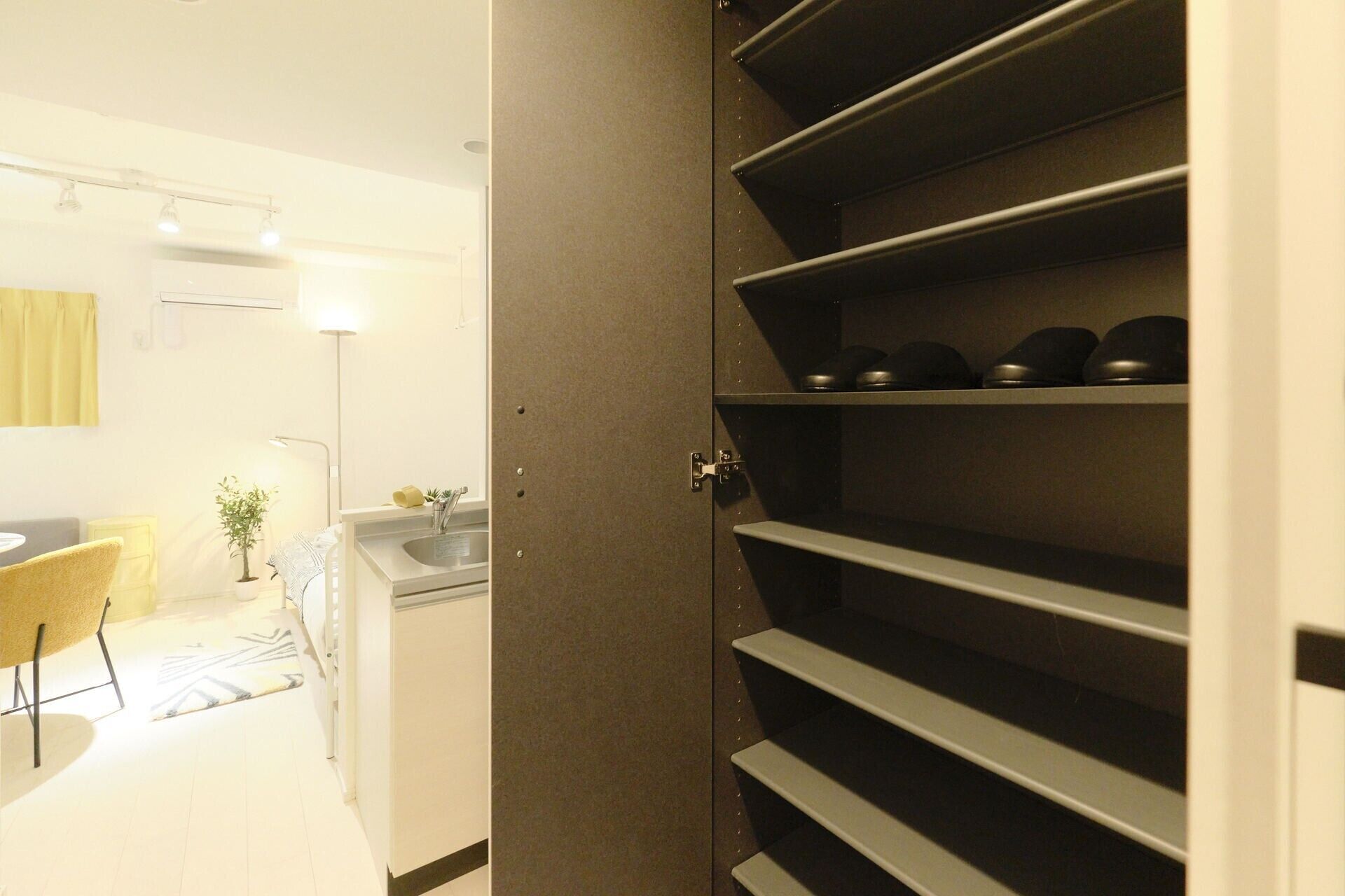 A room with a kitchen area, a dining table with chairs, and a shelving unit with shoes.