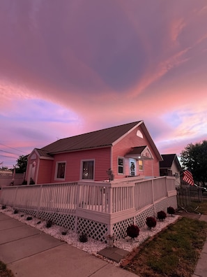 A pink house with a wooden deck, a front porch, and a small garden.