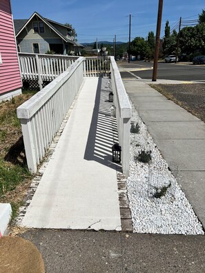 A concrete pathway with a white railing, leading to a residential area with houses and a clear sky.