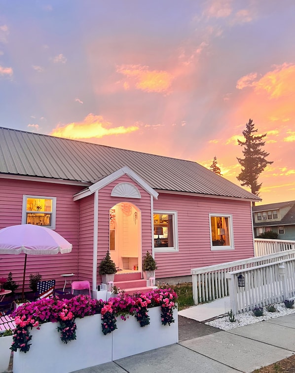 A pink house with a porch, a white railing, and a pink umbrella.