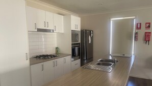 A modern kitchen with white cabinets, stainless steel appliances, a wooden countertop, and a window with a view.