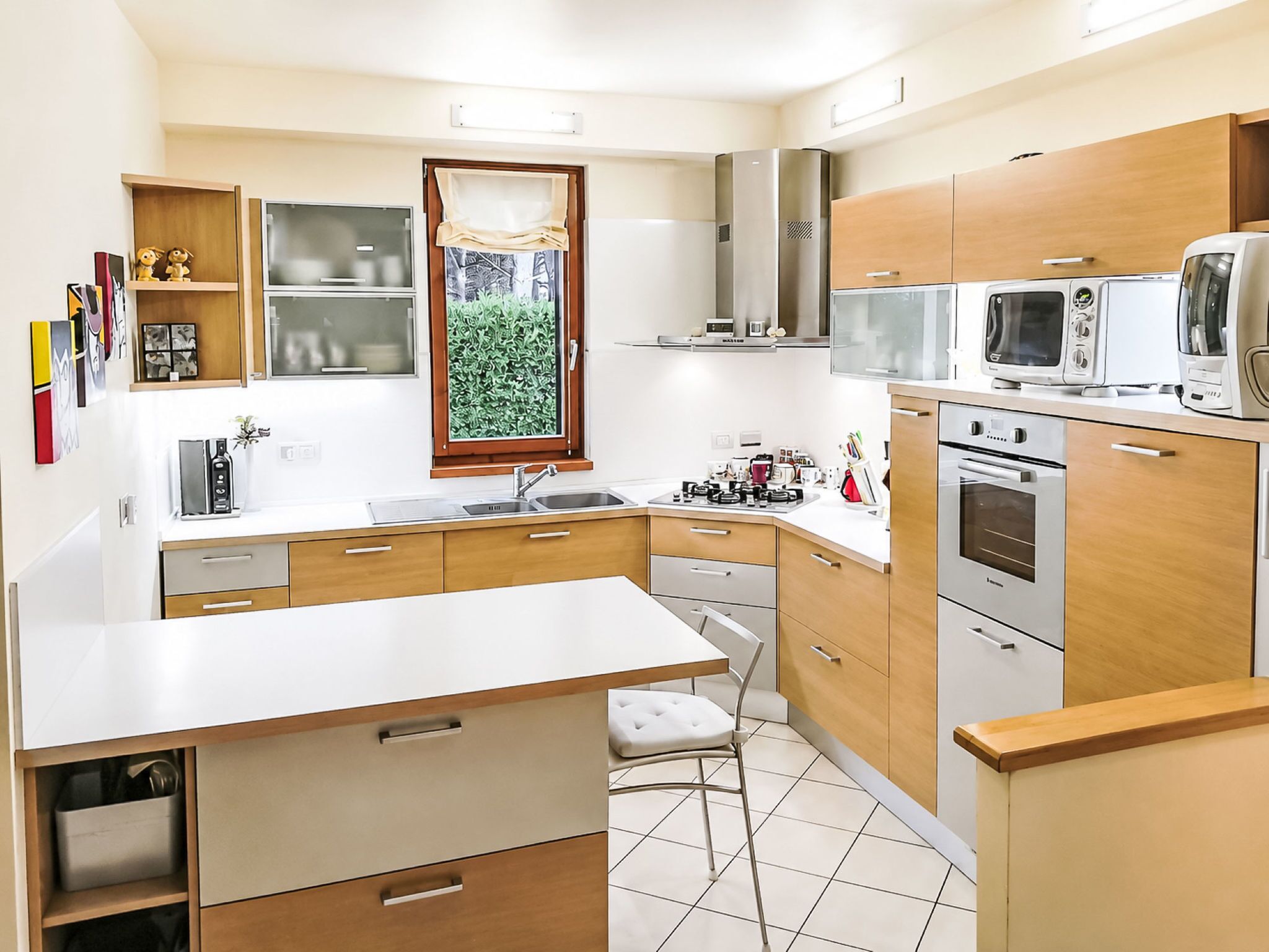A modern kitchen with a central island, built-in appliances, and a window with a view of greenery.