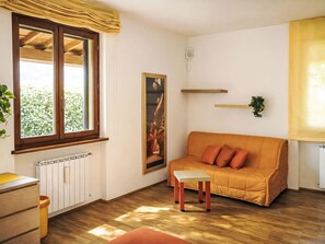 A room with a wooden floor, a sofa with cushions, a radiator, a window with curtains, and a wall-mounted shelf with a plant. - "Casa di Max" by Interhome (Arezzo)