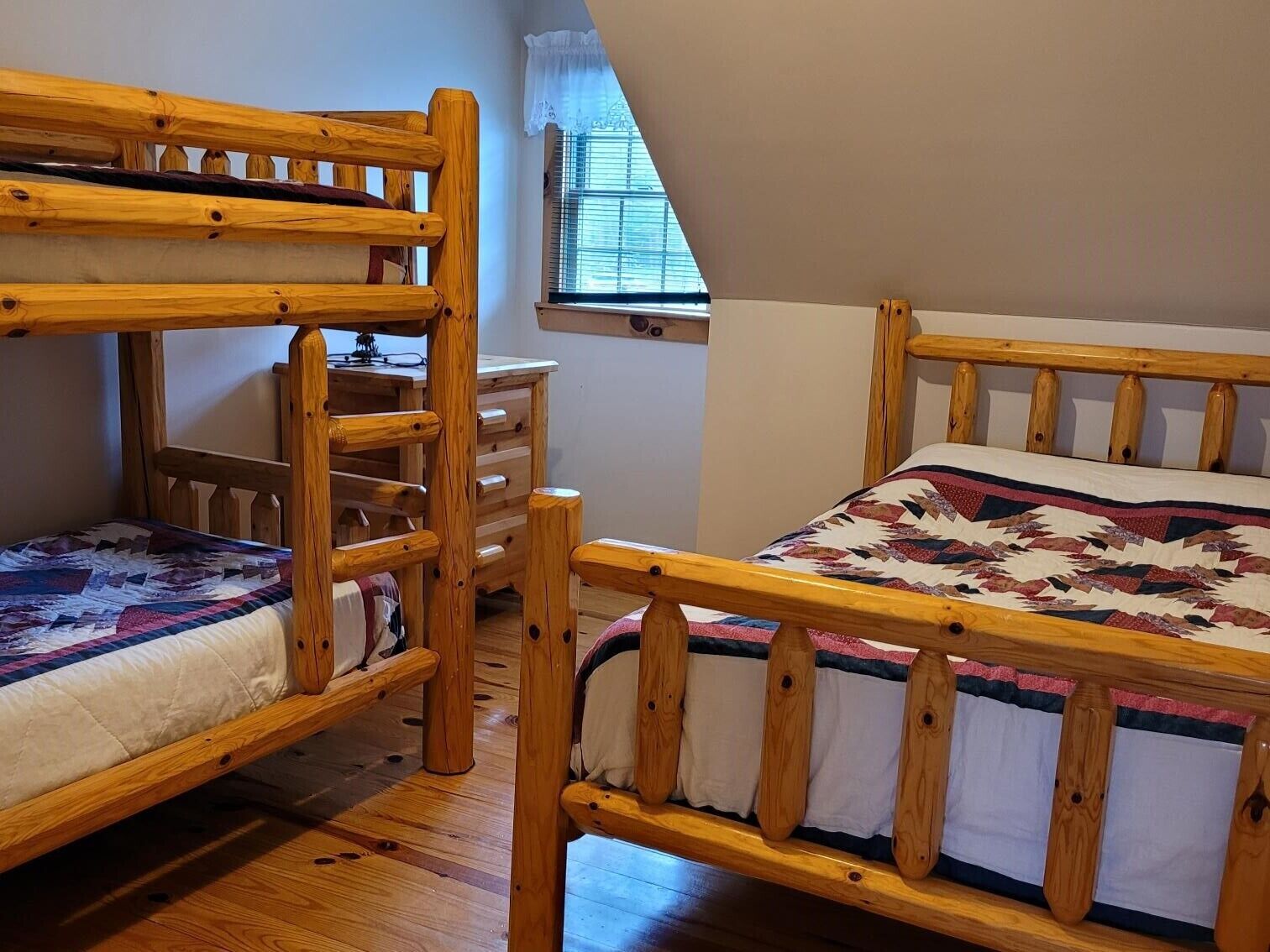 Une chambre avec deux lits superposés, une commode en bois et une fenêtre avec des stores.