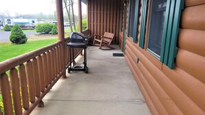 A covered porch with a grill, chairs, and a view of a lake and RVs in the background. - James Creek RV Resort (James Creek)