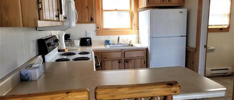 A compact kitchen with wooden cabinets, a white refrigerator, a stove, and a sink.