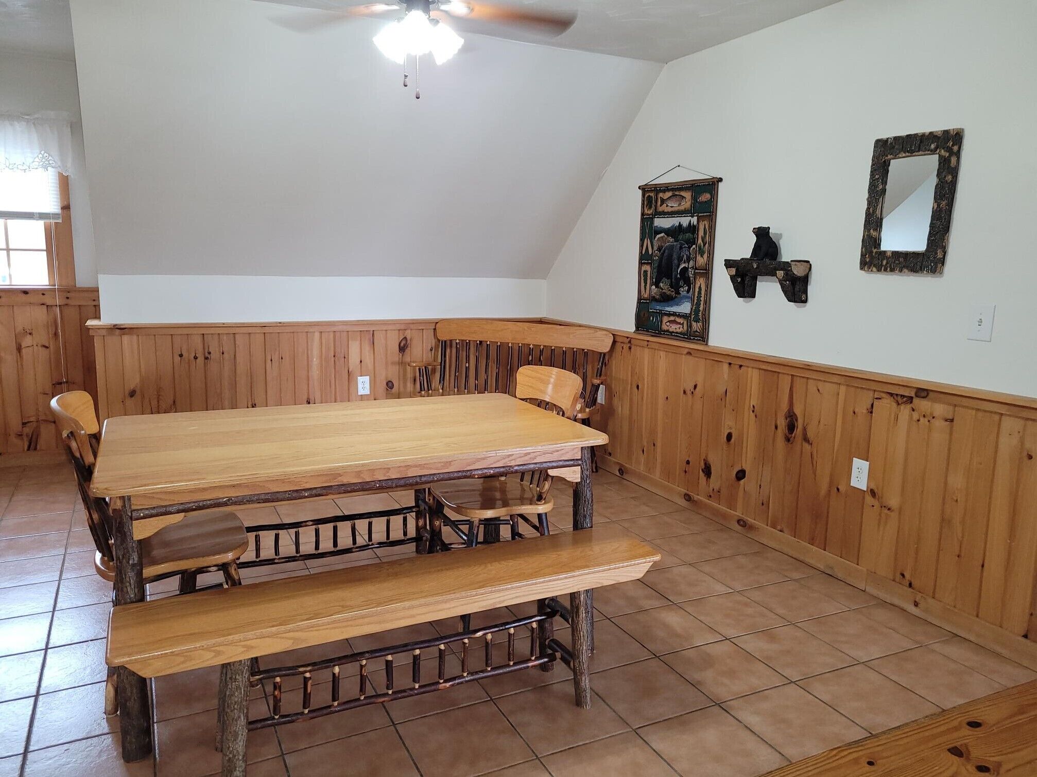 Un espace repas avec une table et des bancs en bois, un ventilateur de plafond et un luminaire fixé au mur.