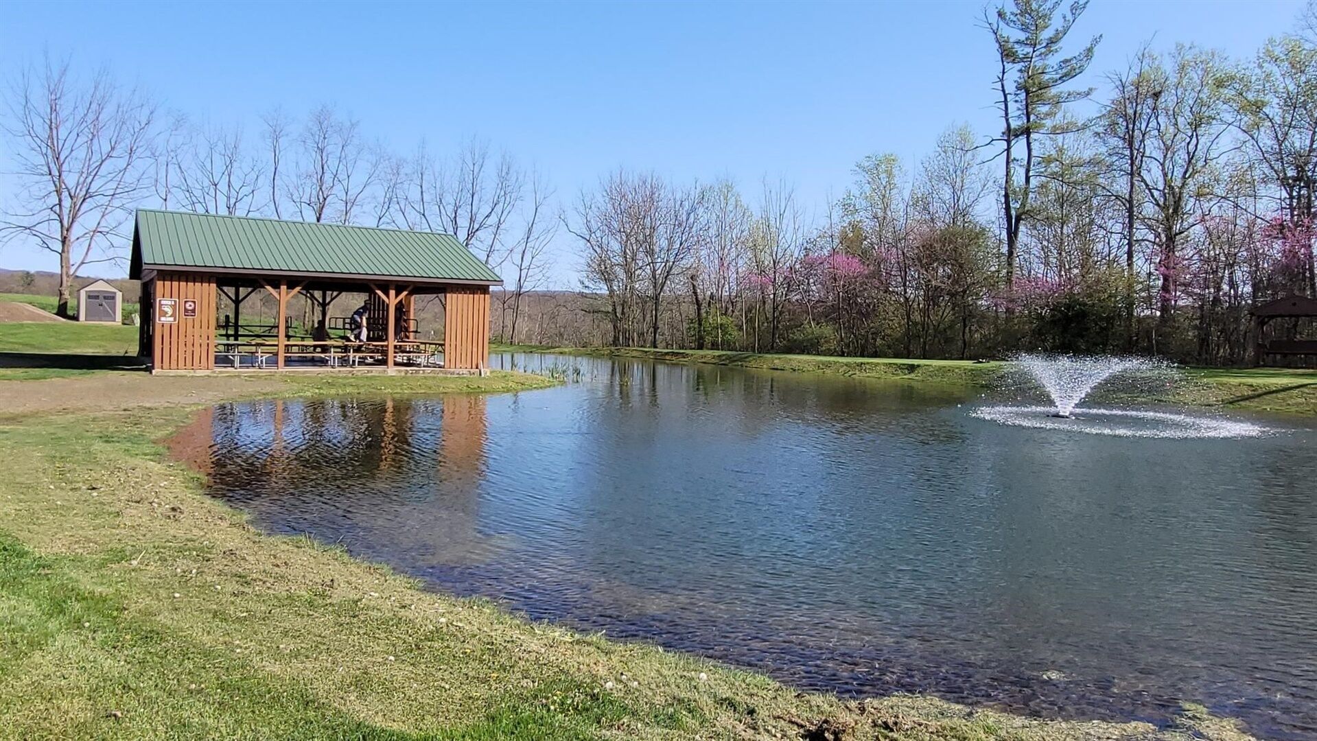 A lakeside pavilion with picnic tables and a small shed.