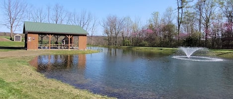 A lakeside pavilion with picnic tables and a small shed.